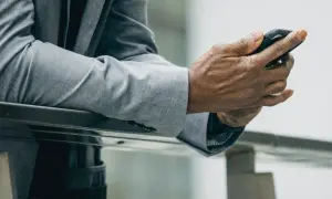Mężczyzna w szarej marynarce i spodniach, trzymający telefon. Idealny zestaw: jaka marynarka do szarych spodni?