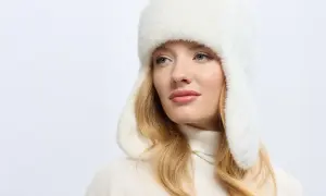 Kobieta w białej, puszystej papasze i golfie, z blond włosami, patrzy w bok.