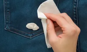 Ręka z papierowym ręcznikiem próbuje usunąć gumę do żucia z dżinsowej kieszeni. Prosty sposób, jak usunąć gumę do żucia z ubrania.