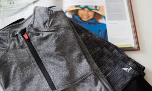 Szara bluza sportowa z zamkiem, wykonana z wytrzymałego poliamidu, leży obok otwartej książki z inspirującym zdjęciem narciarki.