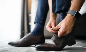 Mężczyzna wiąże eleganckie brązowe buty, a jego granatowe skarpetki w kropki idealnie pasują do garnituru.