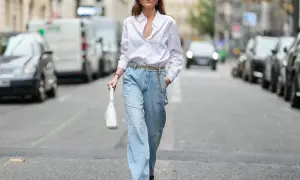 Kobieta w luźnych, jasnych jeansach typu mom fit i białej koszuli, z białą torebką. Idealny look dla każdej kobiety ceniącej wygodę i styl.