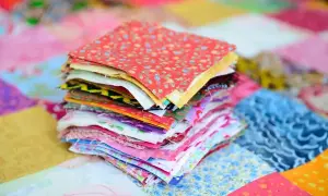 Stos kolorowych kwadratów materiałów, gotowych do stworzenia patchworku. To właśnie patchwork – sztuka łączenia skrawków tkanin w piękne wzory.