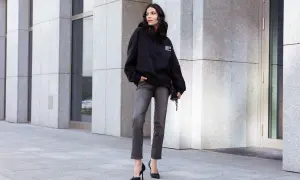 Kobieta w czarnej bluzie z kapturem i szarych jeansach. Luźny krój (loose fit) bluzy zapewnia komfort i swobodę.