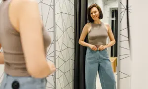 Kobieta w przymierzalni zapina jeansy. Czy rozmiar 27 spodnie damskie to dobry wybór?