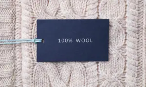 Metka z napisem "100% WOOL" na tle grubego, beżowego swetra w warkocze. To właśnie jest lambswool – czysta wełna.