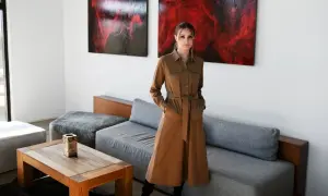 Kobieta w brązowej, casualowej sukience z paskiem stoi w nowoczesnym salonie.