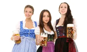 Trzy uśmiechnięte kobiety w tradycyjnych strojach dirndl, trzymające kufle piwa.