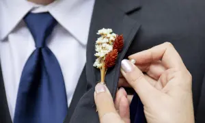 Dłoń przypina do marynarki mały bukiecik z suszonych kwiatów. To właśnie butonierka co to, ozdoba na specjalne okazje.