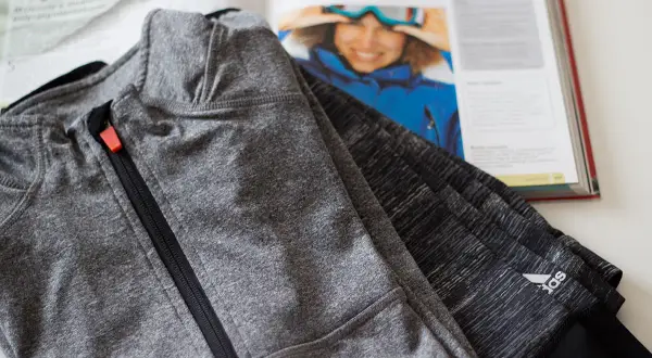 Szara bluza sportowa z zamkiem, wykonana z wytrzymałego poliamidu, leży obok otwartej książki z inspirującym zdjęciem narciarki.
