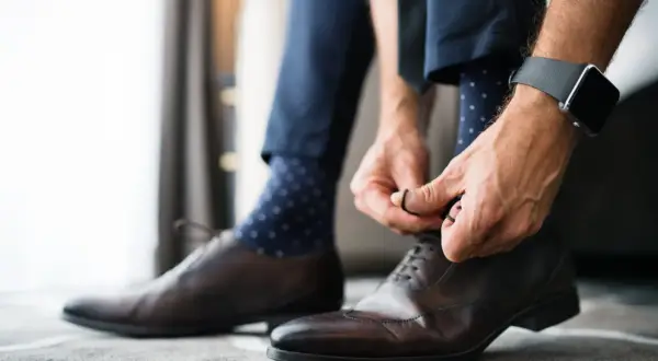 Mężczyzna wiąże eleganckie brązowe buty, a jego granatowe skarpetki w kropki idealnie pasują do garnituru.