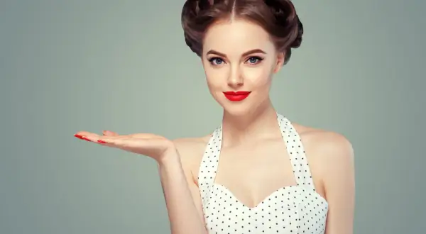Kobieta w stylu pin-up z burzą loków i czerwoną szminką prezentuje coś na otwartej dłoni.