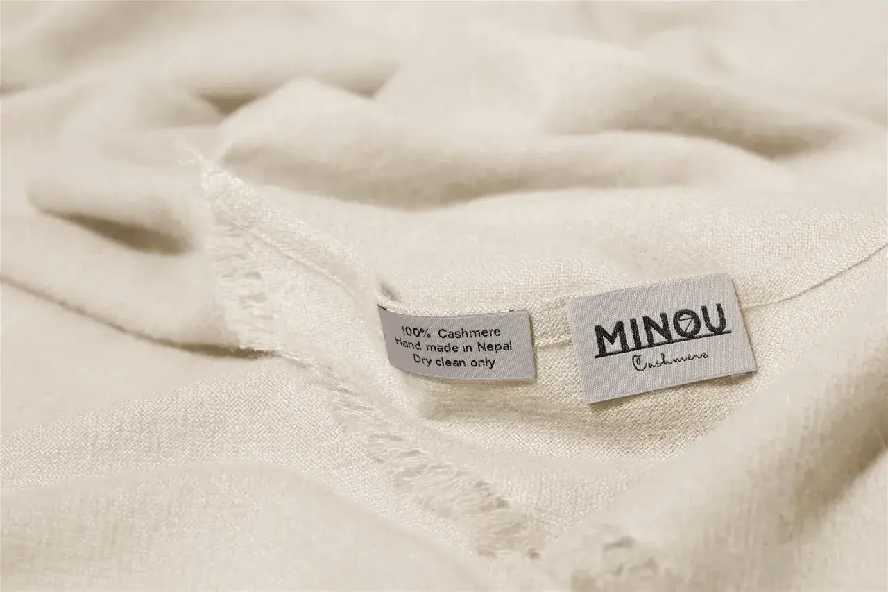 Miękka, kremowa paszmina z metkami: "100% Cashmere, Hand made in Nepal, Dry clean only" i "MINOU Cashmere".