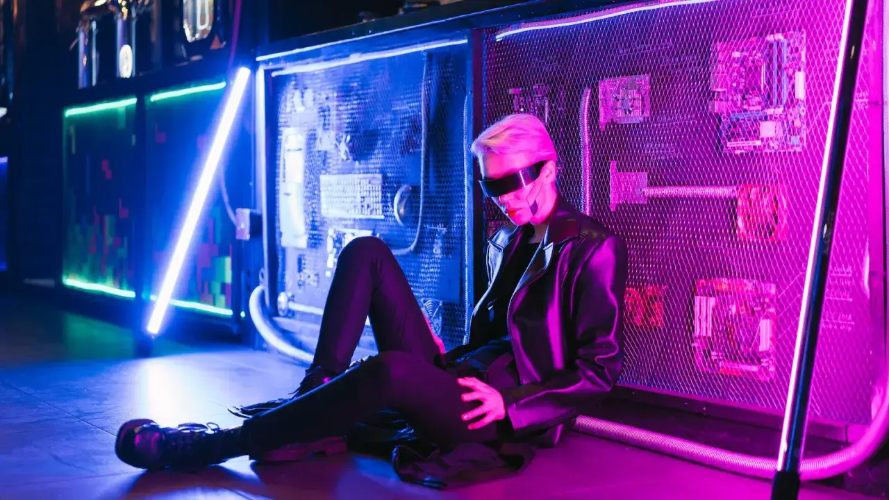 Postać w okularach i skórzanej kurtce siedzi na podłodze w neonowym świetle. Styl cyberpunk.