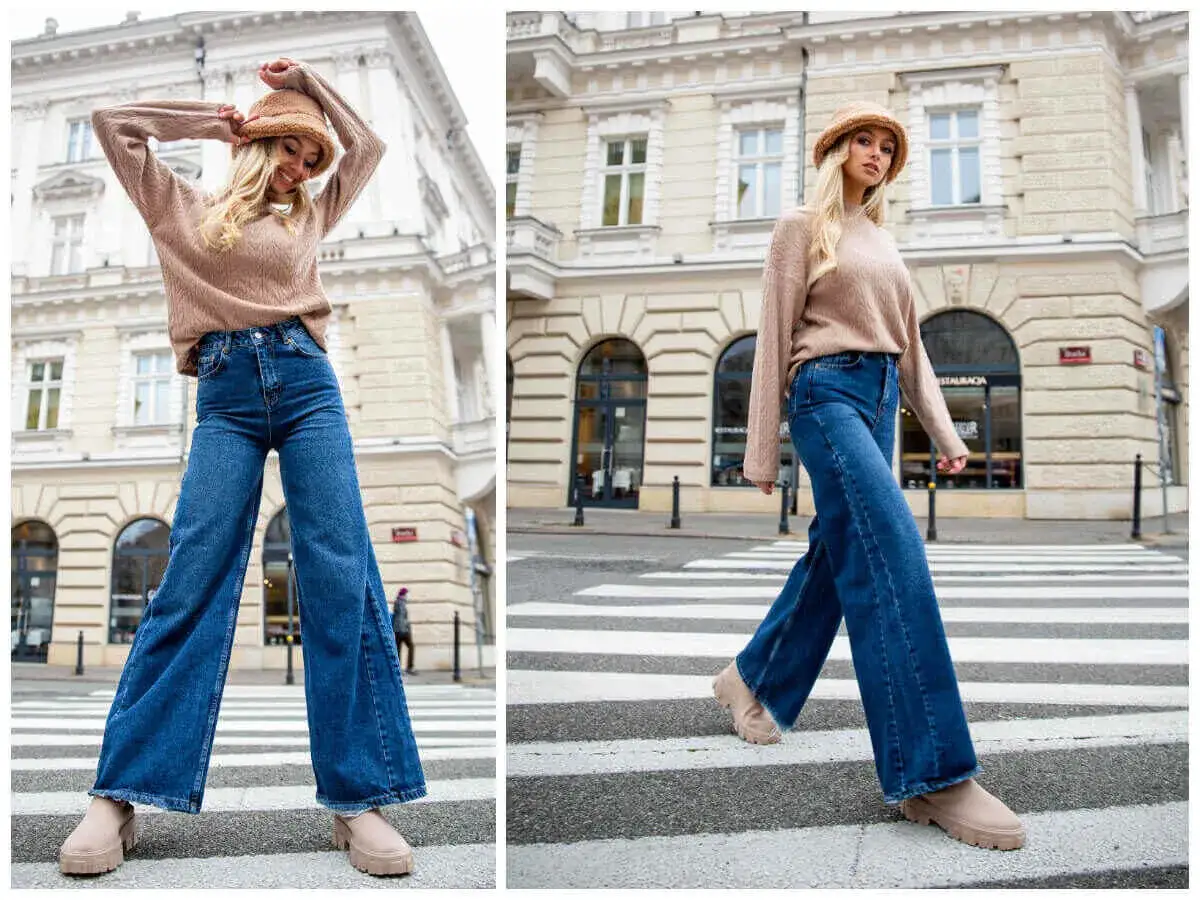 Modna kobieta prezentuje szerokie jeansy stylizacje na tle miejskiej kamienicy. Luźne nogawki i beżowy sweter tworzą stylowy look.