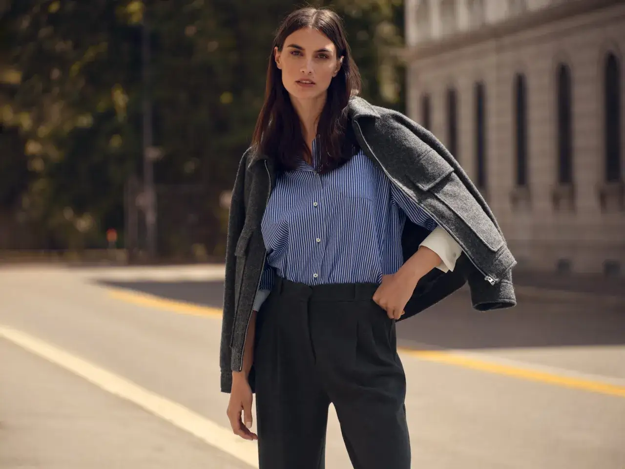 Kobieta w eleganckim stroju, z marynarką narzuconą na ramiona, prezentuje spodnie w kolorze navy.