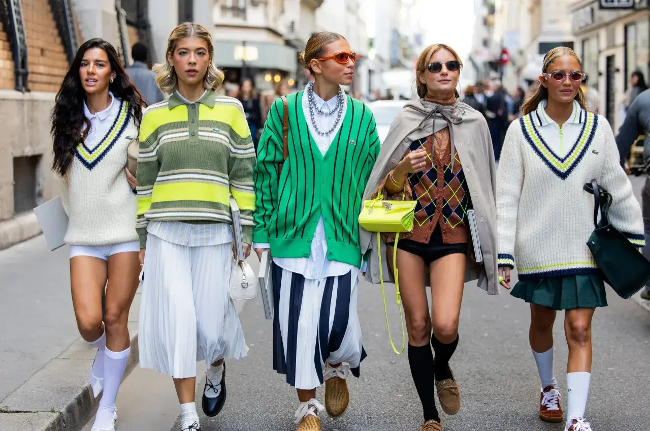 Pięć kobiet w stylu preppy, w swetrach i spódniczkach, idzie ulicą.