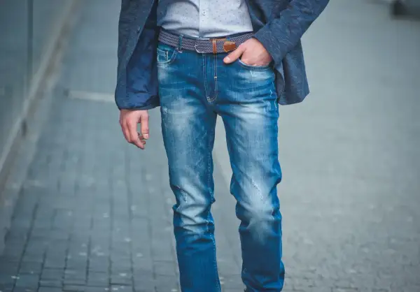 Mężczyzna w niebieskiej marynarce i modnych, przetartych jeansach. Różne rodzaje jeansów męskich można nosić na wiele sposobów.