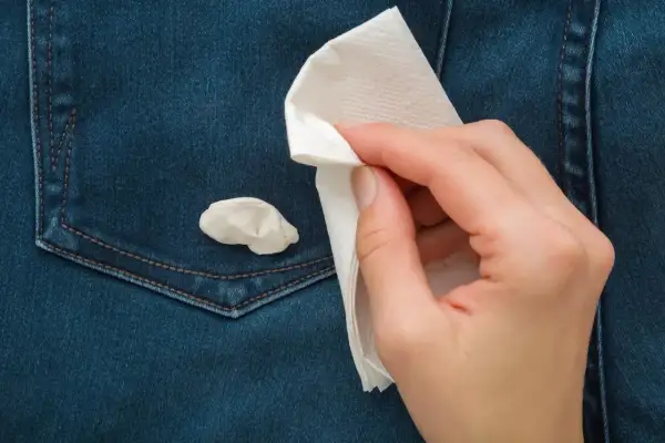 Ręka z papierowym ręcznikiem próbuje usunąć gumę do żucia z dżinsowej kieszeni. Prosty sposób, jak usunąć gumę do żucia z ubrania.