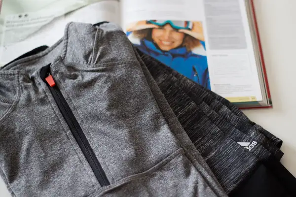 Szara bluza sportowa z zamkiem, wykonana z wytrzymałego poliamidu, leży obok otwartej książki z inspirującym zdjęciem narciarki.