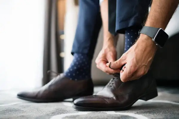 Mężczyzna wiąże eleganckie brązowe buty, a jego granatowe skarpetki w kropki idealnie pasują do garnituru.