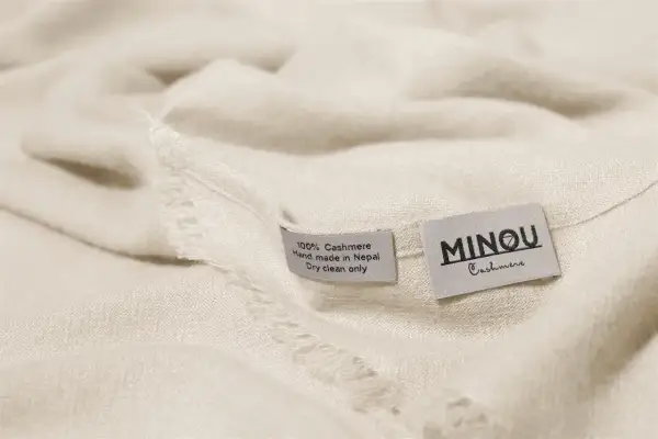 Miękka, kremowa paszmina z metkami: "100% Cashmere, Hand made in Nepal, Dry clean only" i "MINOU Cashmere".