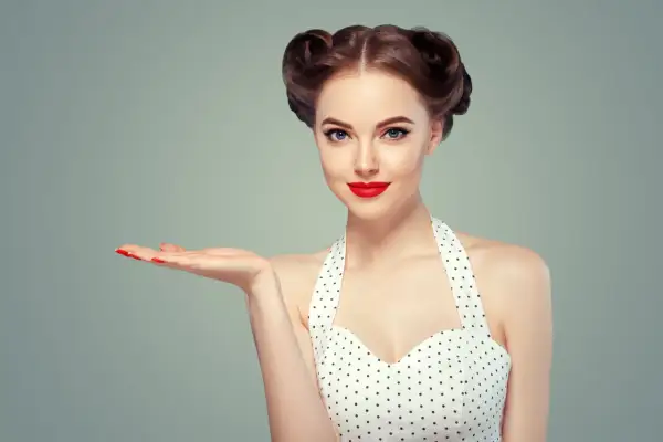 Kobieta w stylu pin-up z burzą loków i czerwoną szminką prezentuje coś na otwartej dłoni.