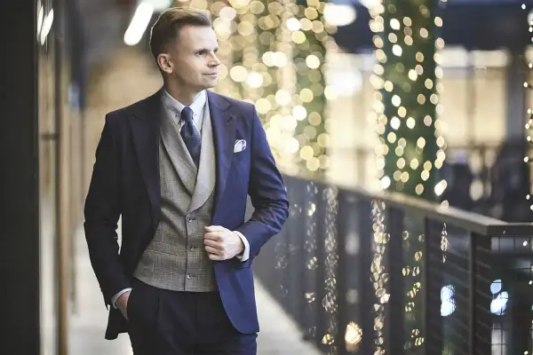 Elegancki mężczyzna w granatowym garniturze, szarej kamizelce i krawacie, gotowy na wieczorne wyjście. Strój koktajlowy męski w pełnej krasie.