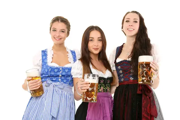 Trzy uśmiechnięte kobiety w tradycyjnych strojach dirndl, trzymające kufle piwa.