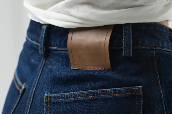 Detale ciemnych jeansów z brązową naszywką. Denim to materiał, z którego są wykonane.
